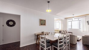 A dining area with a white table and chairs, a clock on the wall, and a painting above the table. - Apt in BC Center w Balcony 260m From Beach Elo0207 (Balneário Camboriú)