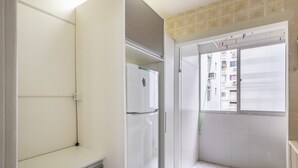 A narrow hallway with a white refrigerator, a small shelf, and a window with blinds. - Apt in BC Center w Balcony 260m From Beach Elo0207 (Balneário Camboriú)