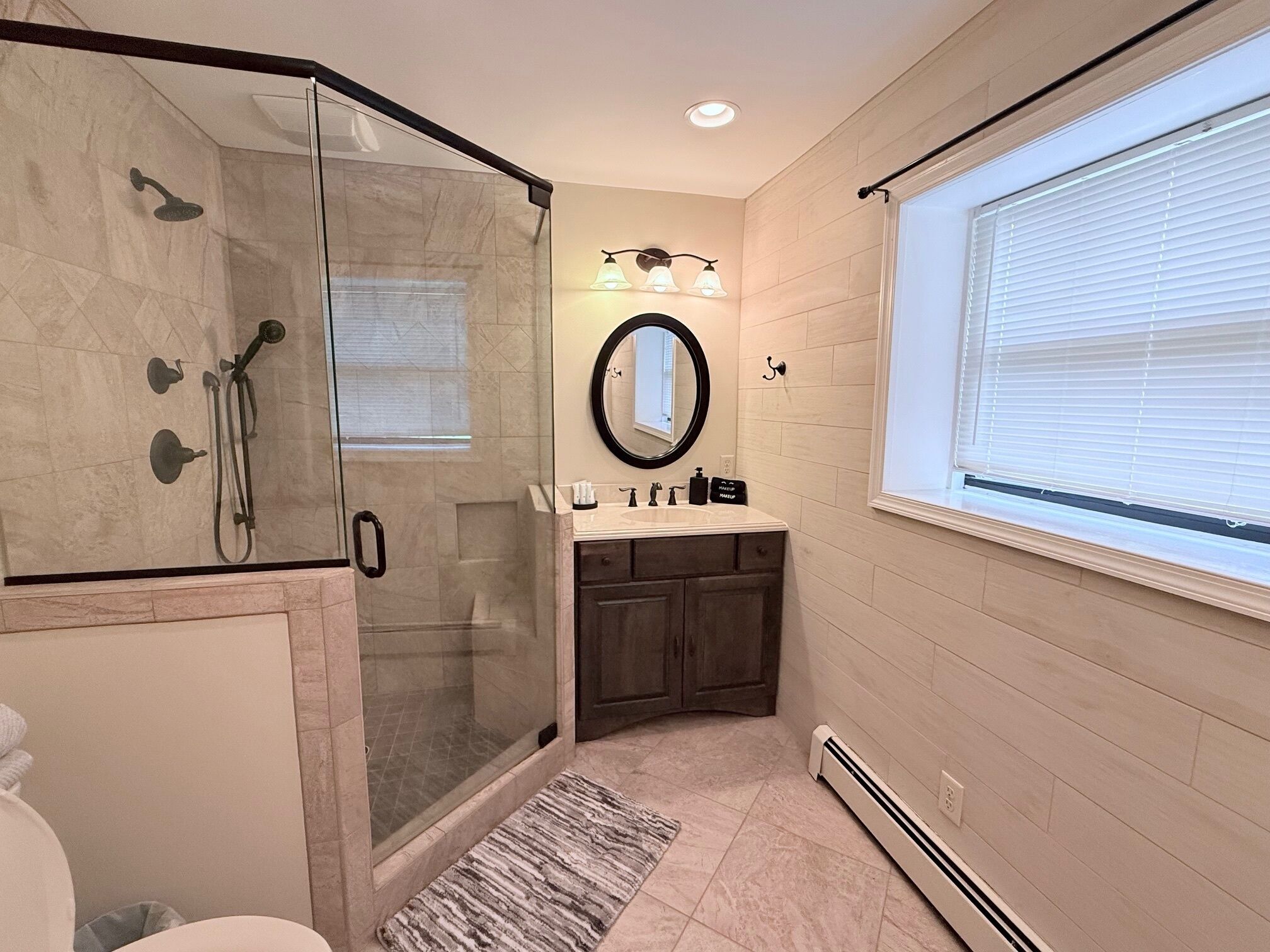 Une salle de bain moderne dotée d’une douche à parois de verre, d’un meuble-lavabo avec miroir et d’une fenêtre laissant entrer la lumière naturelle.