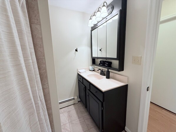 Une salle de bain avec un lavabo blanc, des meubles noirs, un miroir avec éclairage intégré et une serviette posée sur le comptoir.