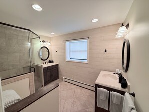 Une salle de bain moderne dotée d’une douche à parois de verre, d’un meuble-lavabo avec miroir et d’une fenêtre laissant entrer la lumière naturelle.