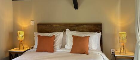 Un dormitorio con techo de madera, una cama grande con ropa de cama blanca y naranja, y dos lámparas de noche.