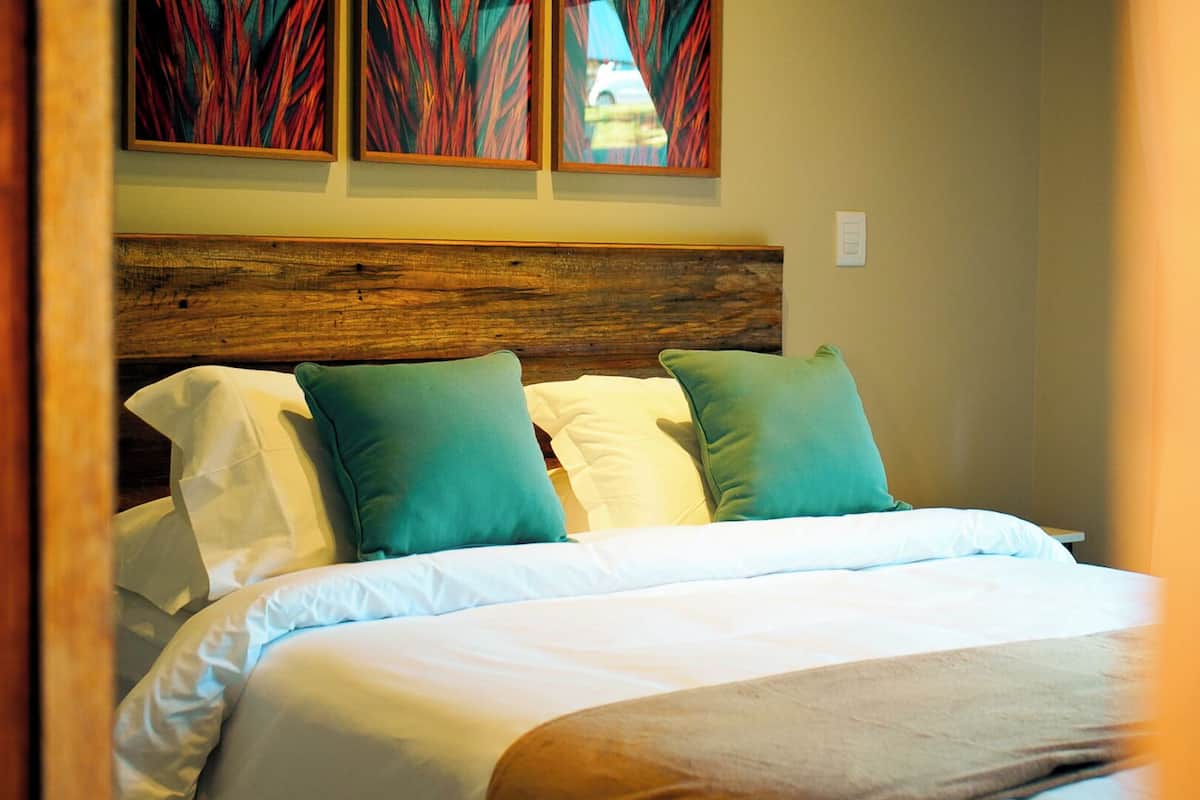 Un lit bien fait, avec des oreillers blancs et turquoise, une tête de lit en bois et un tableau accroché au-dessus.