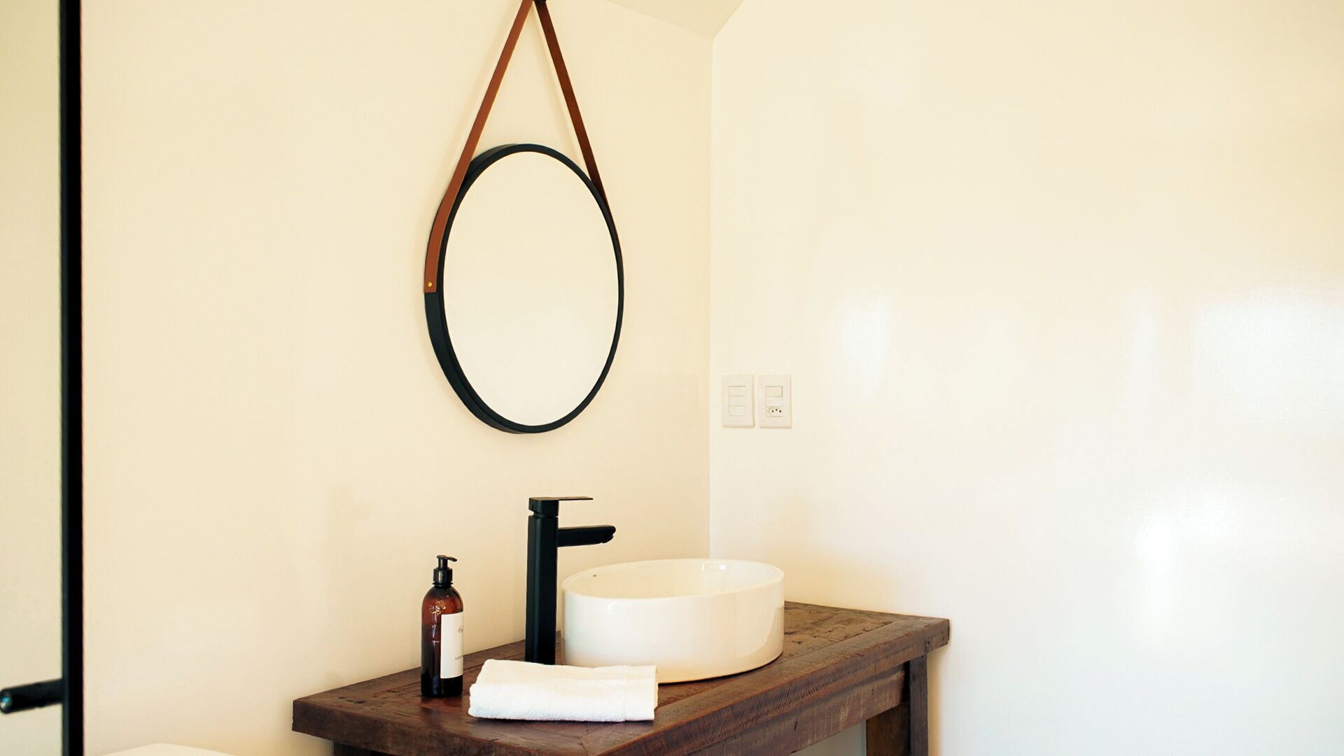A bathroom with a round mirror, a black faucet, a white sink, and a wooden countertop.