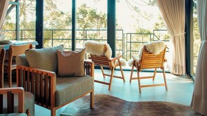 Una sala de estar moderna con un sofá, dos sillones de madera con mantas de piel, una mesa de centro de madera y un ventanal con cortinas.