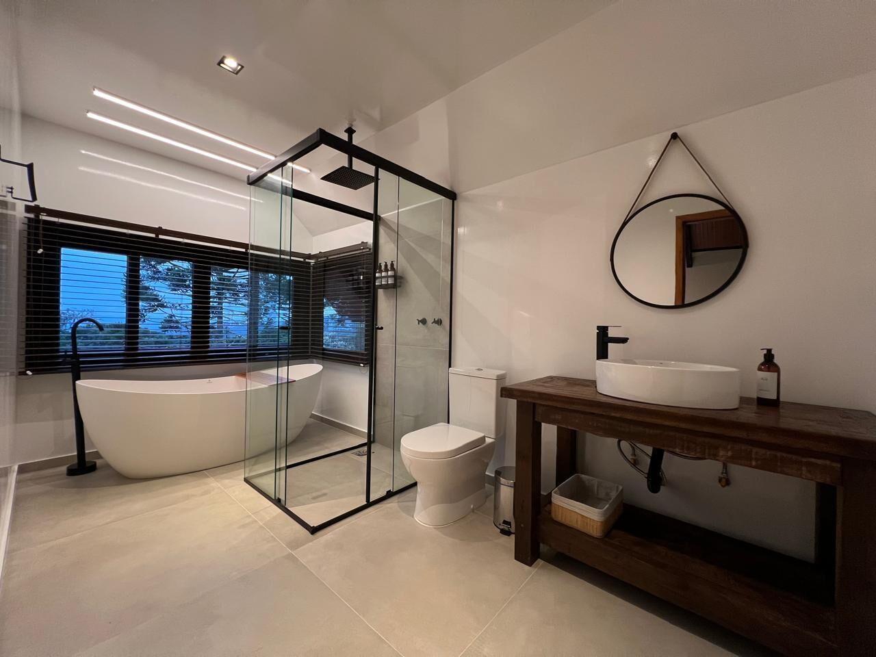 Une salle de bain moderne dotée d’une douche à parois de verre, d’une baignoire sur pieds, de toilettes et d’un meuble-lavabo en bois avec un évier et un miroir.