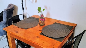 Ein Holztisch mit zwei gewebten Tischsets, einer Glaskaraffe mit Pflanze und einer Lampe.