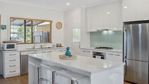 A modern kitchen with white cabinetry, stainless steel appliances, and a central island with bar stools. - Jacks Corner - Moments to the beach, free wifi, pet friendly - wont be disapointed! (Normanville)