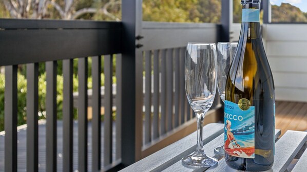 A bottle of wine and two glasses on a wooden table on a balcony with a railing.