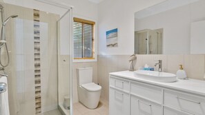 Ein modernes Badezimmer mit Duschkabine aus Glas, Toilette, Waschbecken mit Spiegel und Fenster mit Jalousien.