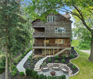 A two-story log cabin with a balcony, a stone fire pit, and a landscaped garden.