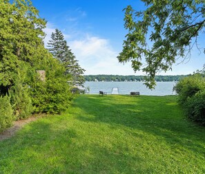 A grassy area with two chairs facing a lake, surrounded by trees and a wooden structure.