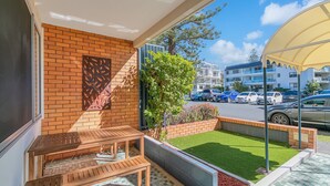 A balcony with a wooden bench, a brick wall, and a view of a parking area with cars and buildings. - Blue Pacific 2 - Beachside Tugun Unit - Linen Provided - Min. 3 Nights! (Tugun)