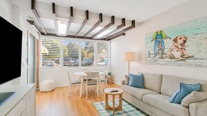 A modern living room with a dining area, a sofa, a TV, and a painting on the wall. - Blue Pacific 2 - Beachside Tugun Unit - Linen Provided - Min. 3 Nights! (Tugun)
