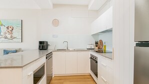 A modern kitchen with white cabinets, a built-in oven, a coffee maker, and a sink. - Blue Pacific 2 - Beachside Tugun Unit - Linen Provided - Min. 3 Nights! (Tugun)