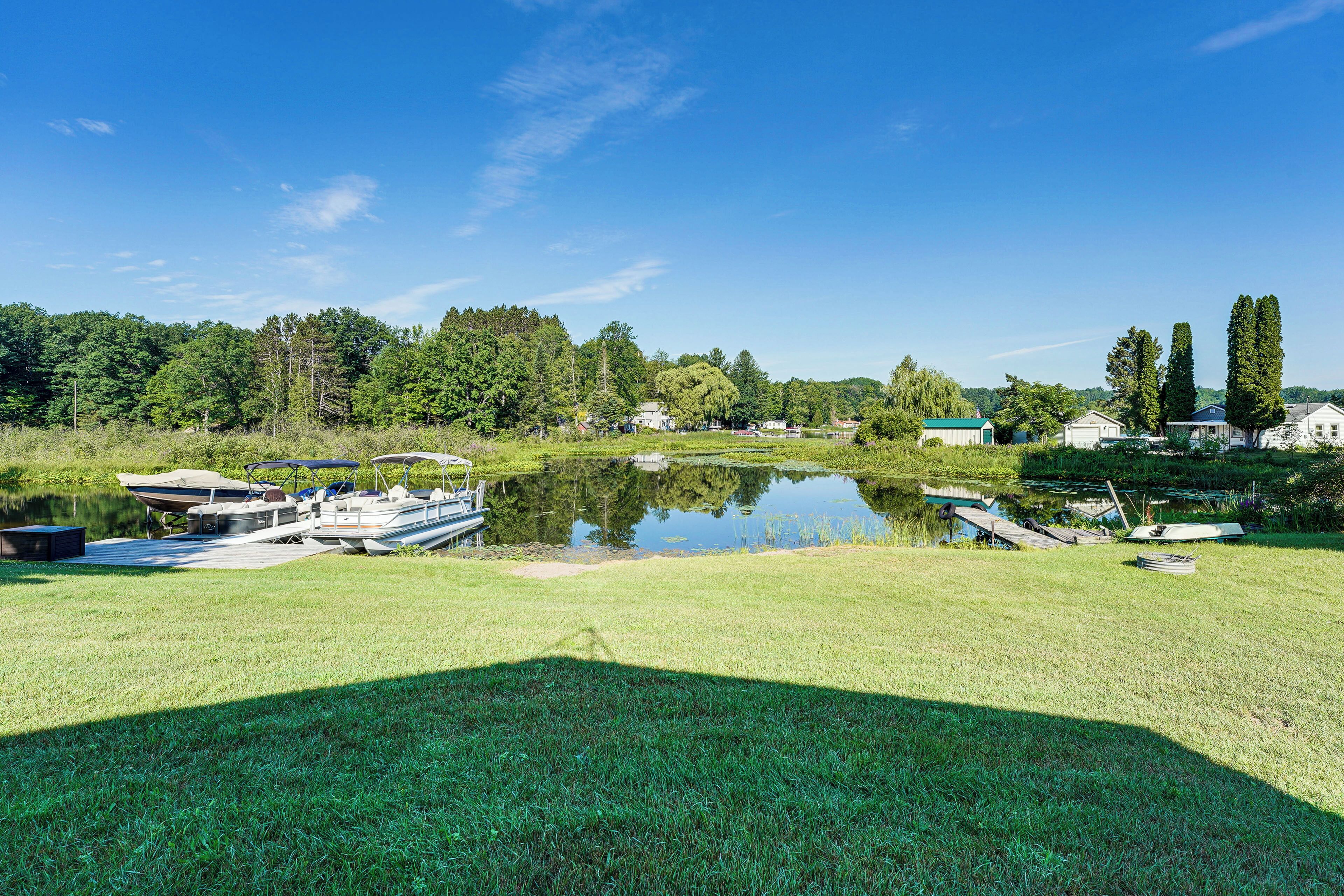 A serene lakeside setting with boats docked near the water's edge, surrounded by lush greenery and a clear blue sky.
