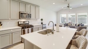 Una cocina moderna con una isla central, electrodomésticos de acero inoxidable y un comedor con mesa y sillas blancas.