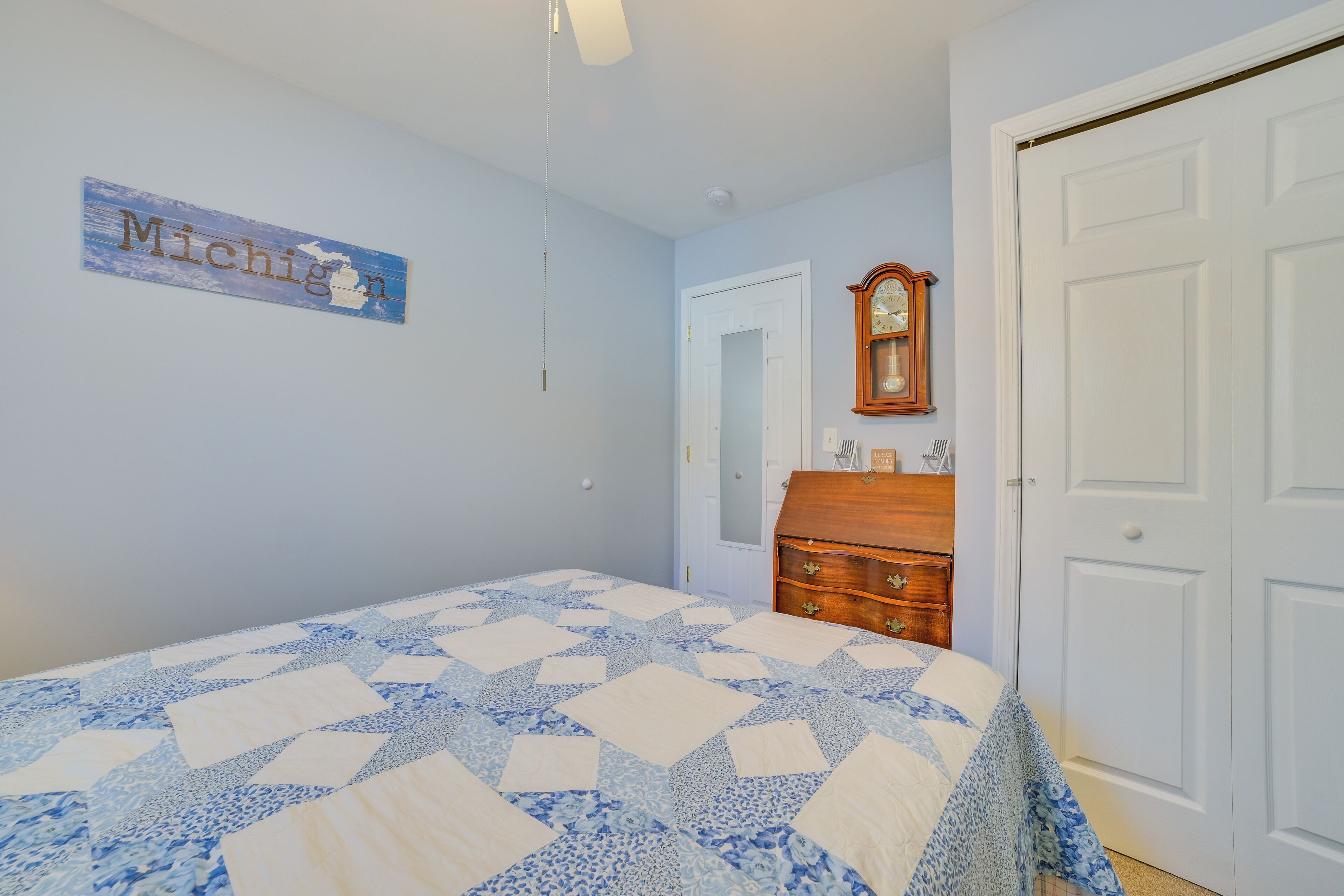 A bedroom with a bed, a dresser, a clock, and a wall sign.