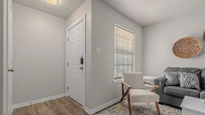Un salón con sofá gris, sillón blanco, una mesita pequeña y un adorno redondo tejido en la pared.