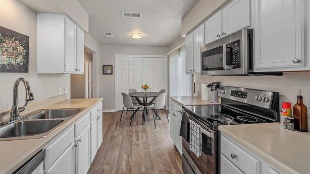 Una cocina moderna con armarios blancos, electrodomésticos de acero inoxidable y piso de madera.