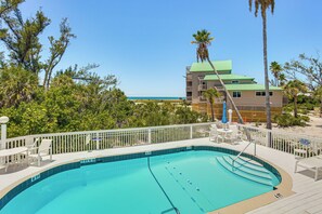 Ein Pool mit Blick auf Strand und Meer, umgeben von Palmen und einer eingezäunten Poolterrasse.