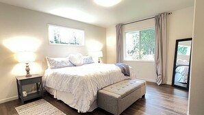 A bedroom with a bed, bedside lamps, a bench, a rug, a window with curtains, and a mirror. - Luxury 3BR Home + Game Room - Wooded Escape Near Downtown Redmond (Redmond)