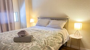 A neatly made bed with floral bedding, two bedside lamps, and a rolled towel on the bed.