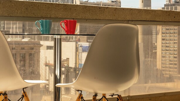 A balcony with two white chairs and a table, overlooking a cityscape with a prominent tower.