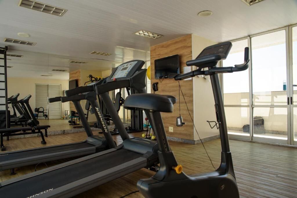 Un gimnasio con cintas de correr, un televisor montado en la pared y ventanas amplias.