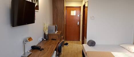 Quarto de hotel com televisão de tela plana, escrivaninha com luminária, micro-ondas, cama e porta que dá para outro cômodo.