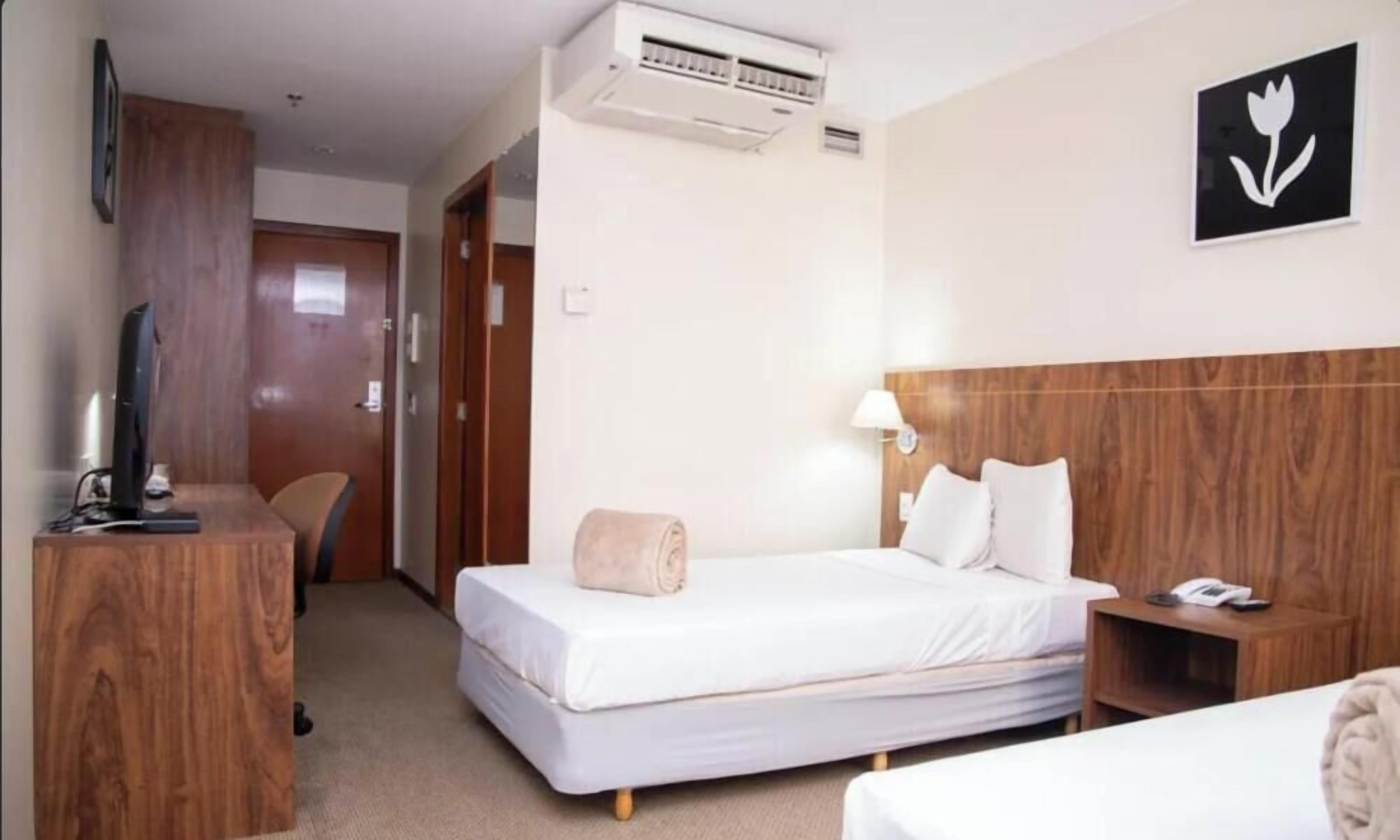 Una habitación de hotel con cama, mesita de noche, lámpara y televisor sobre un mueble.