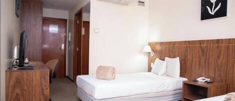 A hotel room with a bed, bedside table, lamp, and a TV on a stand.
