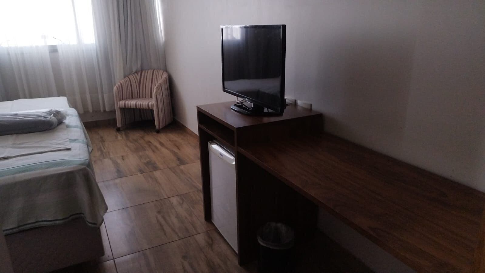 Une chambre d’hôtel avec un lit, une chaise, une télévision et un petit réfrigérateur.
