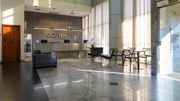 A modern hotel lobby with a reception desk, seating area, and large windows.