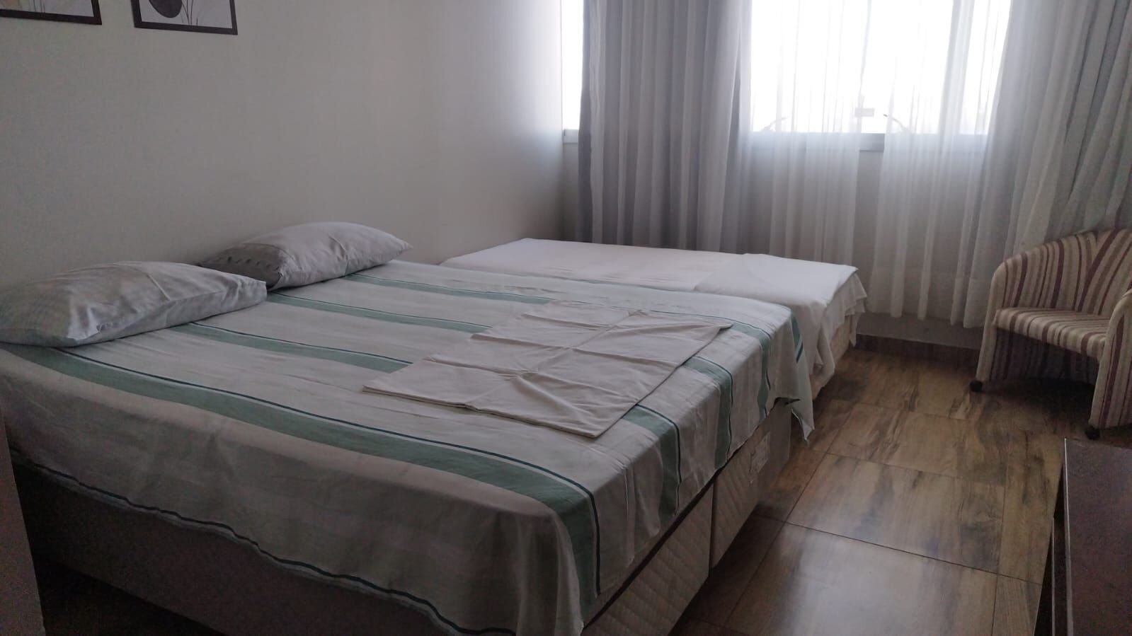 Habitació amb dos llits, una cadira i una finestra amb cortines.