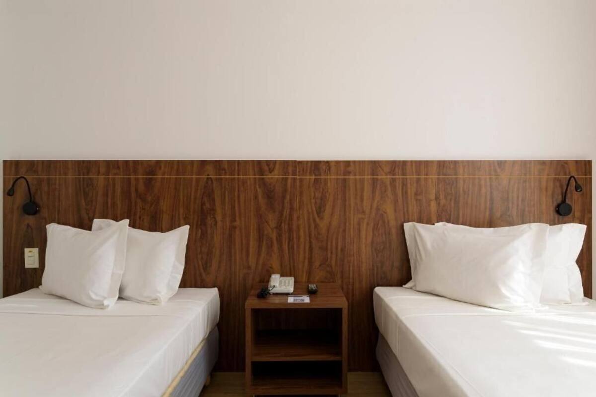 A hotel room with two beds, a wooden headboard, bedside lamps, and a small nightstand with a phone.