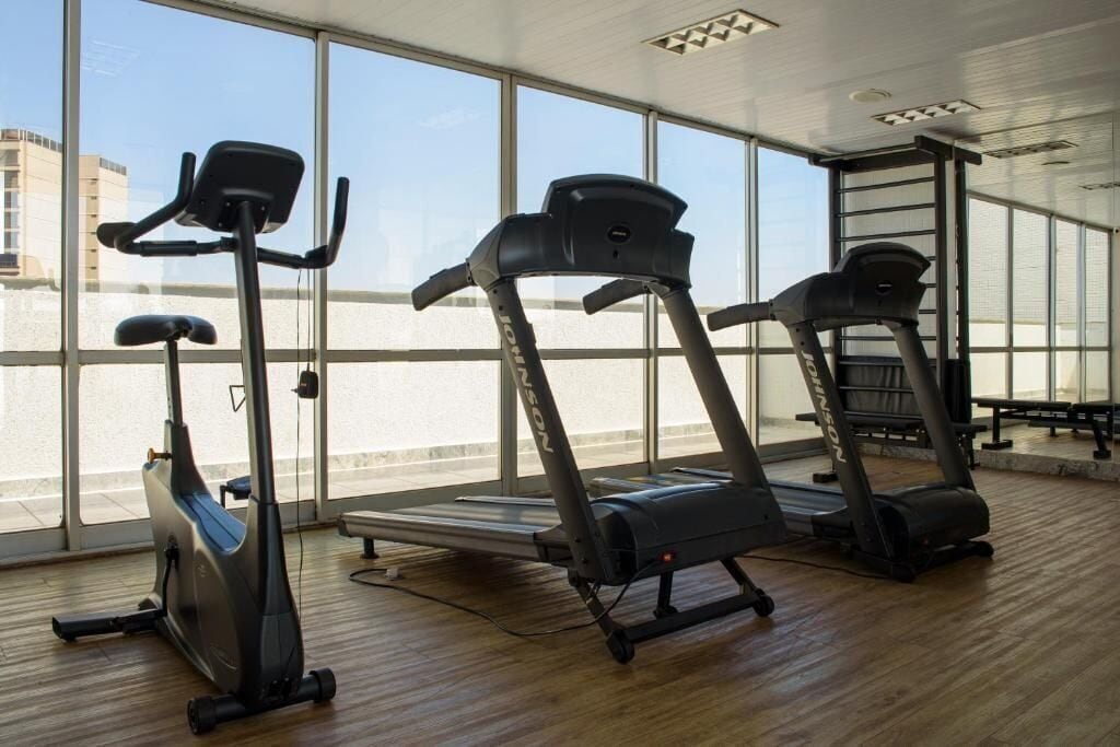 A gym with stationary bikes, treadmills, and a large window with a view of buildings.