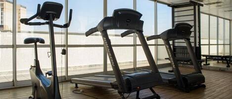 Un gimnasio con bicicletas estáticas, cintas de correr y un amplio ventanal con vistas a edificios.
