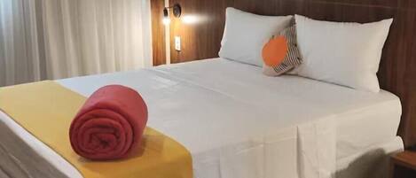 A hotel room with a bed, a nightstand, a lamp, and a window with curtains.