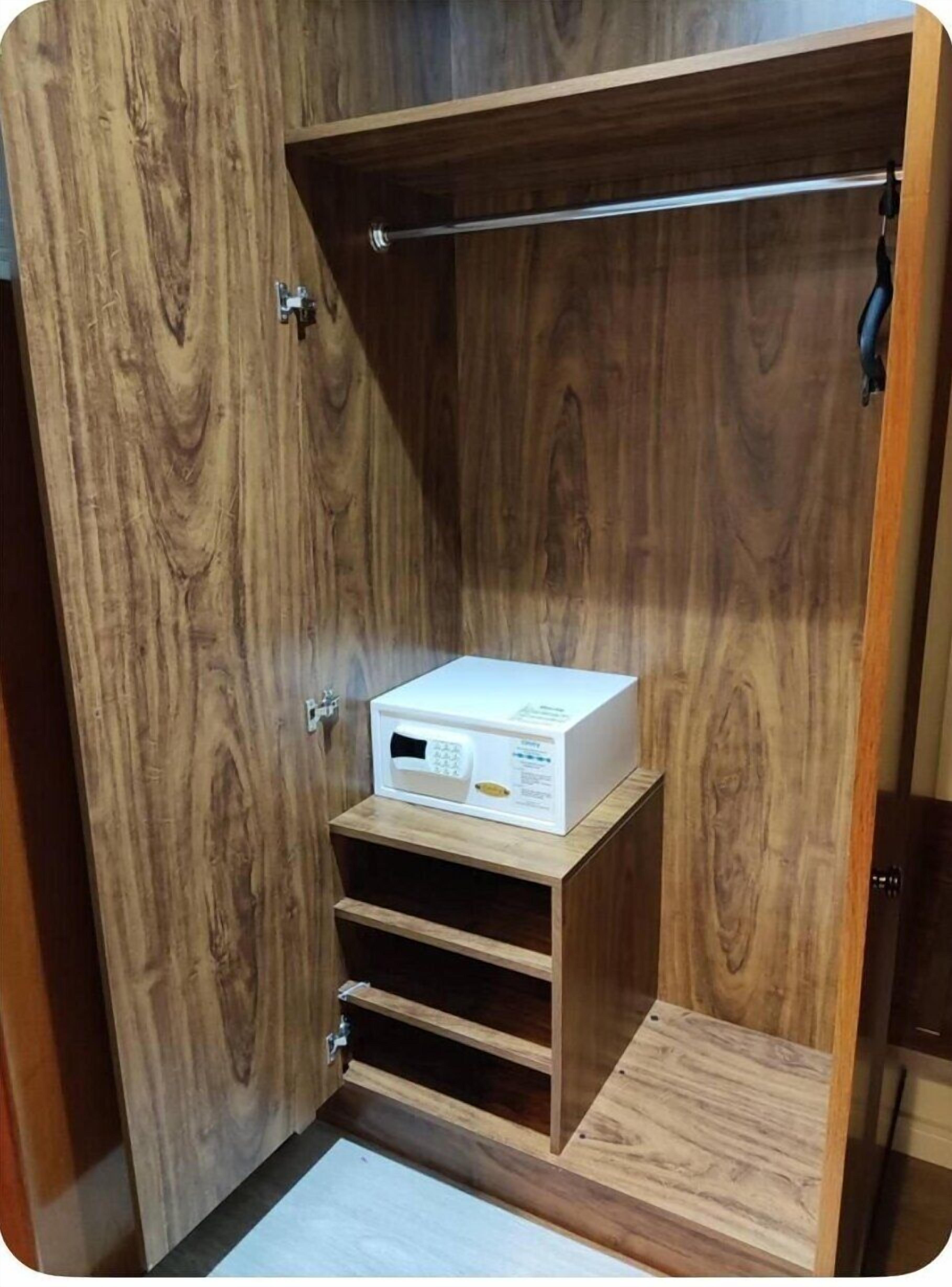 A wooden closet with a microwave on a shelf, a hanging rod, and a small step for accessibility.