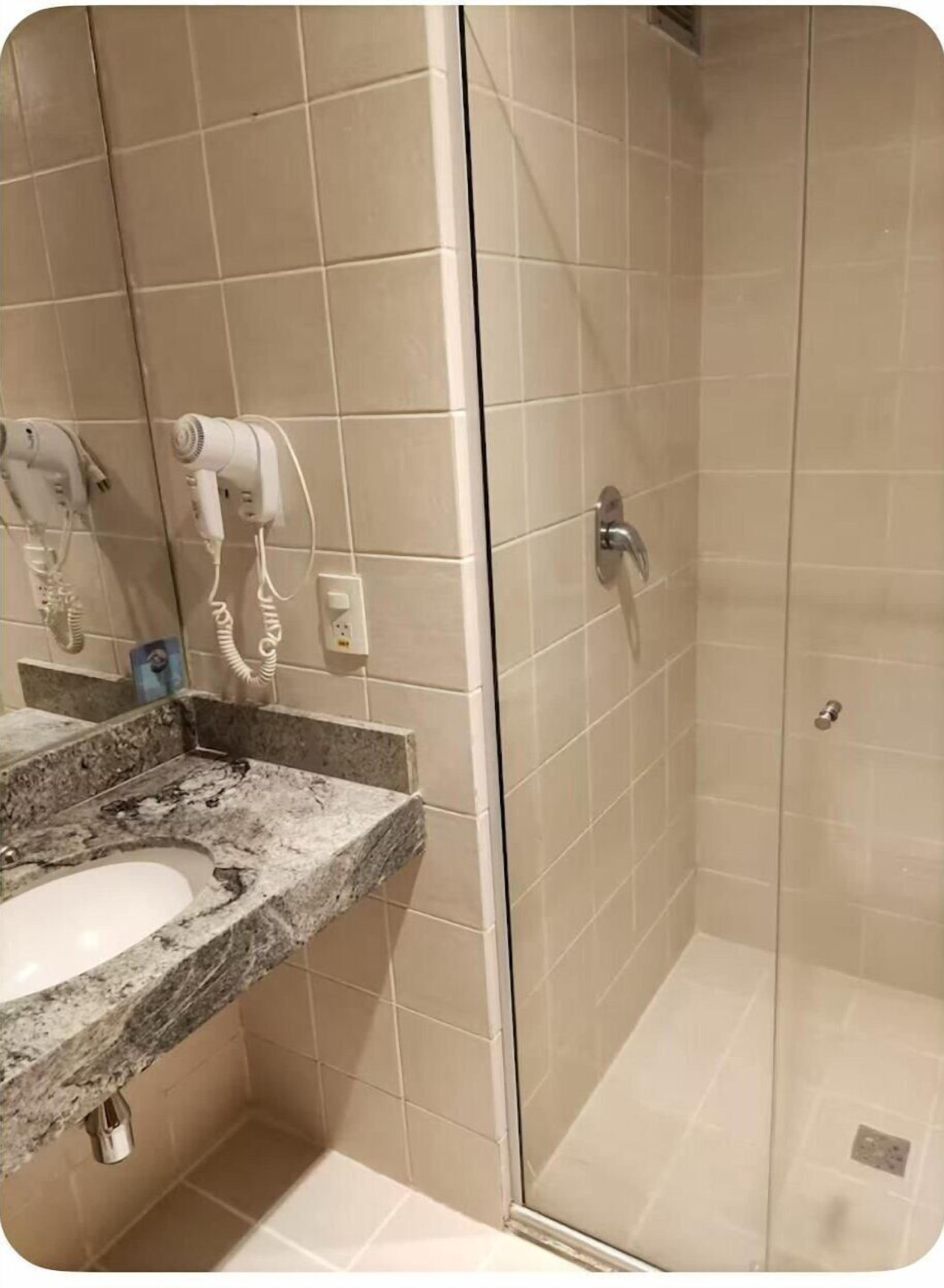 A bathroom with a granite countertop, a sink, a shower with a glass door, and two hair dryers mounted on the wall.