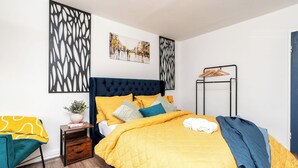 Um quarto moderno com uma cama grande, uma mesa de cabeceira com uma planta e uma obra de arte pendurada na parede.