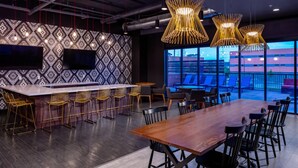 A modern conference room with a long wooden table, black chairs, a bar area with stools, and a patterned wall. - Sleepover | Vibrant Studio - Downtown Des Moines (Des Moines)