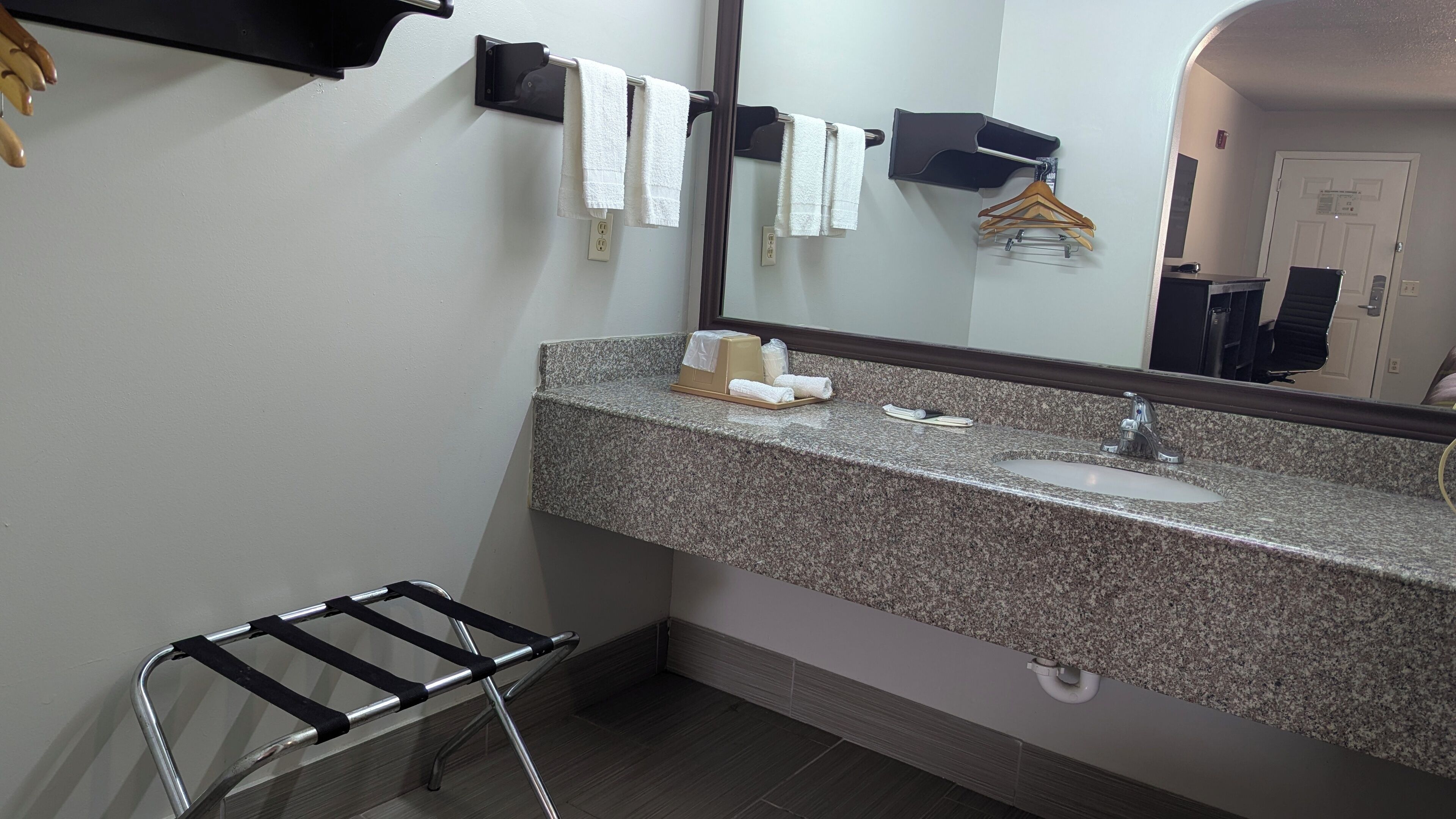 Un baño con encimera de granito, lavamanos, espejo, toallero y tendedero para toallas.