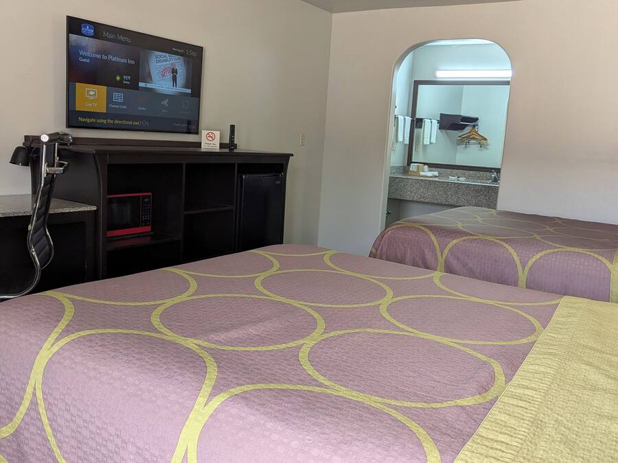 A hotel room with two beds, a TV mounted on the wall, a microwave, and a small desk.
