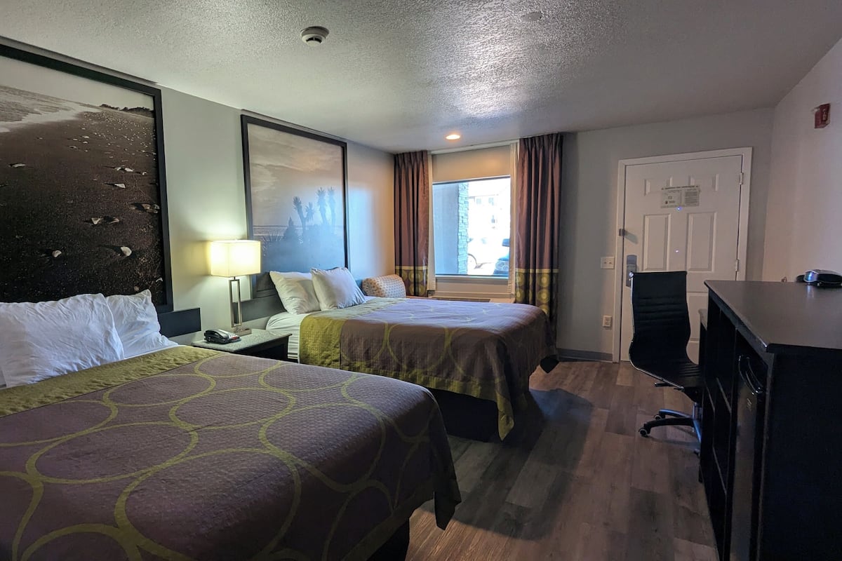 A hotel room with two beds, a desk, a chair, a lamp, and a window with curtains.