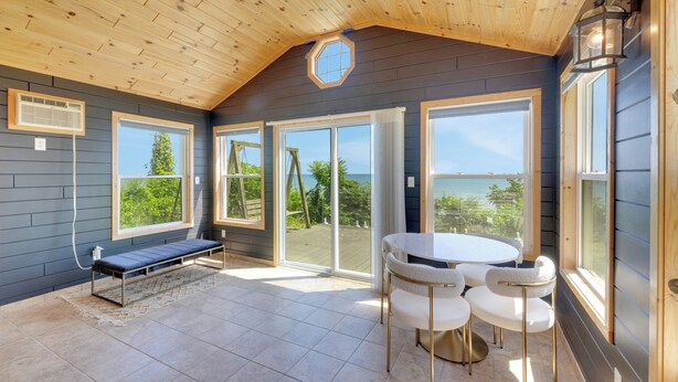 A spacious room with a high ceiling, a round table with chairs, a bench, and large sliding glass doors leading to an outdoor area. - Perfect 5-bedroom house with private beach, indoor pool, in charming Carsonville (Carsonville)