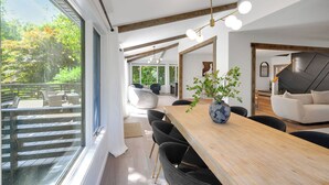 A modern dining area with a wooden table, black chairs, and a vase with greenery. There is a large window with a view of outdoor furniture and trees. - Perfect 5-bedroom house with private beach, indoor pool, in charming Carsonville (Carsonville)