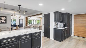 A modern kitchen with dark cabinetry, a marble countertop, and a built-in coffee station. - Perfect 5-bedroom house with private beach, indoor pool, in charming Carsonville (Carsonville)