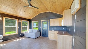 A spacious living area with a white couch, a kitchen with wooden cabinets, and large windows offering a view of the outdoors. - Perfect 5-bedroom house with private beach, indoor pool, in charming Carsonville (Carsonville)